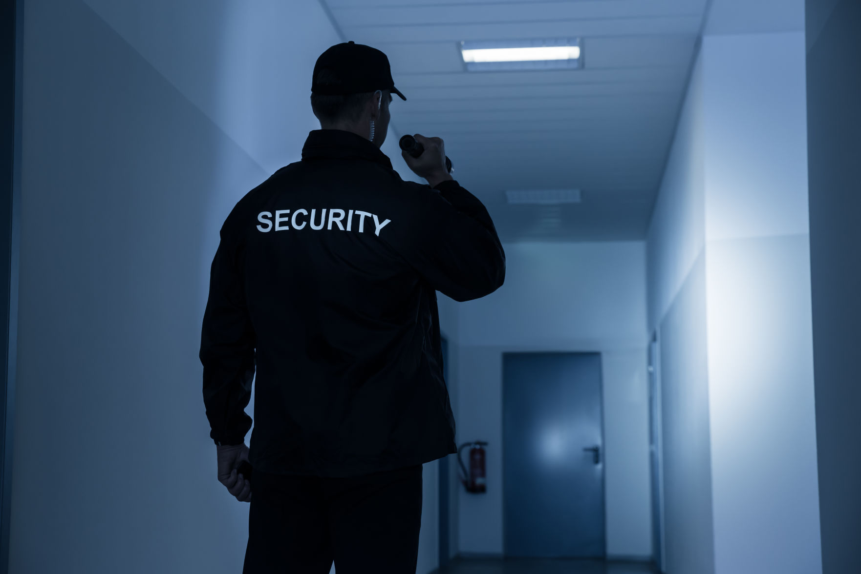 Security Guard With Flashlight In Building Corridor